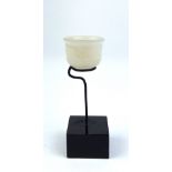 AN INDIAN CARVED JADE MINIATURE CUP Carved with flutes to base, on a black perspex stand. (approx