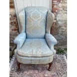 AN EARLY 20TH CENTURY WING ARMCHAIR Fashioned in the Georgian style, in blue floral fabric