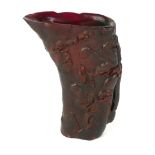 A CHINESE CARVED HORN LIBATION CUP Red stained with carved decoration of figures in a mountainous