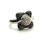 A 14CT WHITE GOLD, BLACK AND WHITE DIAMOND RING The cluster of diamonds in a half twist edged with