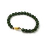 AN EARLY 20TH CENTURY YELLOW METAL AND JADE BRACELET With a fish form clasp and a single strand of