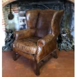 A GEORGIAN STYLE TAN LEATHER WING ARMCHAIR Complete with loose cushion, raised on square oak