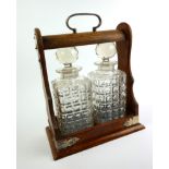 AN EDWARDIAN OAK AND CUT LEAD CRYSTAL GLASS TANTALUS Having a single carry handle with silver plated