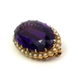 A VICTORIAN YELLOW METAL, AMETHYST AND SEED PEARL BROOCH The faceted oval cut stone edged with