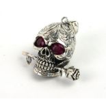 A WHITE METAL AND RUBY GLASS SKULL AND ROSE PENDANT Having scrolled decoration with faceted ruby