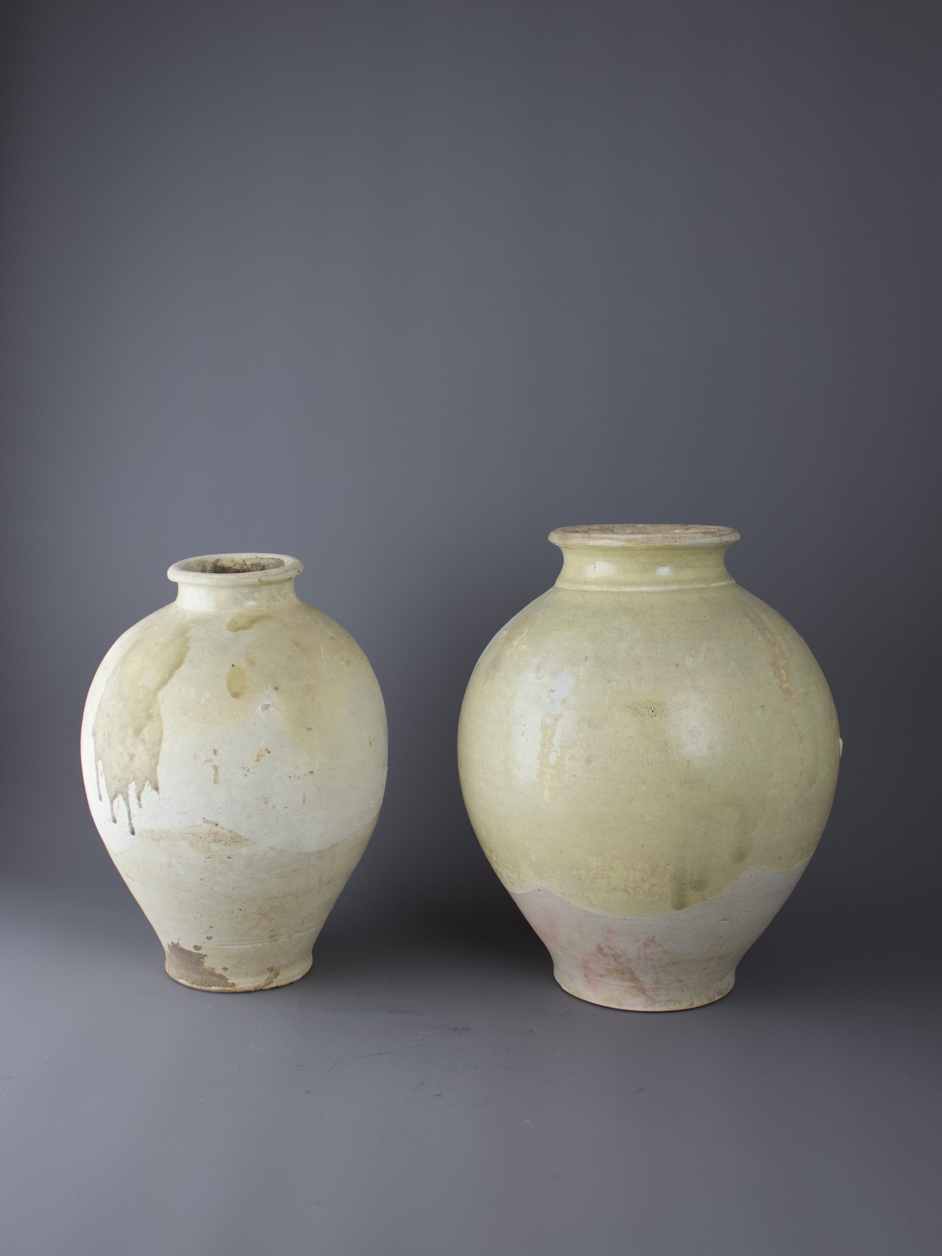 Two strawglazed ovoid Pottery Jars, Tang Dynasty H27cm and H24cm with the glaze stopping short of