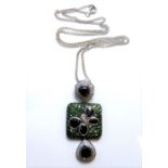 A contemporary coloured diamond and green garnet pendant, the central square plaque set with green