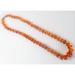 An Art Deco period lady's amber necklace; the spherical graduated faceted beads ranging from 14mm