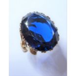 A 9-carat yellow-gold ring, the large oval blue stone claw set above an ornate gallery and bow