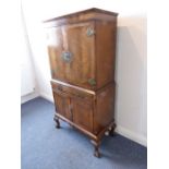 A mid-20th century walnut drinking cabinet in earlier style; two cross-banded doors with ornate