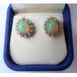 A pair of opal and diamond-set cluster earrings, each oval opal cabochon within a surround of twelve