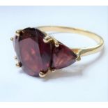 A three-stone garnet ring; the central oval mixed-cut garnet flanked by a triangular garnet, the