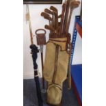 A canvas and leather golf bag containing a wide variety of golf clubs and woods (mostly hickory-