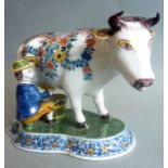 An early 20th century Makkum pottery Delftware model of a farmer in wide-brimmed hat milking a