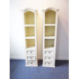 A pair of tall and slim display units; arched tops above three shelves each with three drawers