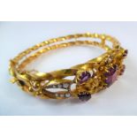 An Edwardian amethyst, half pearl and 9 carat gold hinged bangle, the top section of the openwork