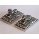 A pair of heavy Art Deco period cast chrome onto brass paperweights modelled as recumbent lions on