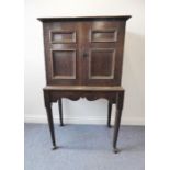 An 18th century oak cabinet-on-stand; the two hinged panelled doors opening to reveal an arrangement