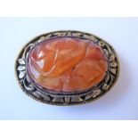 A Chinese hardstone clip brooch, the central oval carved agate within the scrolling foliate bezel,