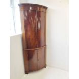 A late 18th century bow-fronted mahogany free standing corner cupboard; the dentil cornice above two