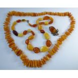Two amber bead and 'nugget' necklaces, one further and an oval amber brooch within a scrolling