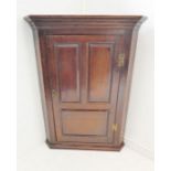 A mid-18th century hanging oak corner cupboard; single door with three fielded panels and brass H-