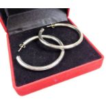 A pair of large silver hoop earrings within a red velvet presentation box