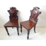 A pair of mid-19th century mahogany hall chairs; ornately carved backs on turned tapering front