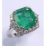An emerald and diamond-set cluster ring, the rectangular cut cornered emerald claw-set above the