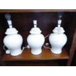 A set of three baluster-shaped cream ceramic table lamps (34cm high excluding electrical fitting)