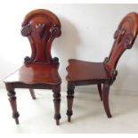 A pair of mid-19th century mahogany hall chairs; carved backs above serpentine-fronted seats and