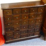 An antique bank of thirty elm drawers; each with circular brass handle, raised on plinth base (