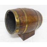 An early 20th century brass coopered oak barrel mounted on an angular oak base; the barrel with a