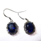 A pair of silver earrings of oval form, each with a hand-cut cobalt-blue stone surrounded by white