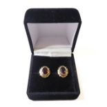 A pair of 9-carat yellow gold earrings, each centrally set with a hand-cut dark-red oval stone (