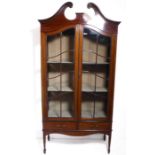 An early 20th century mahogany and boxwood-strung display cabinet; the broken swan-neck pediment