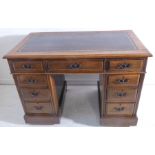 A late 19th century oak pedestal desk; the gilt-tooled leather inset top over an arrangement of nine