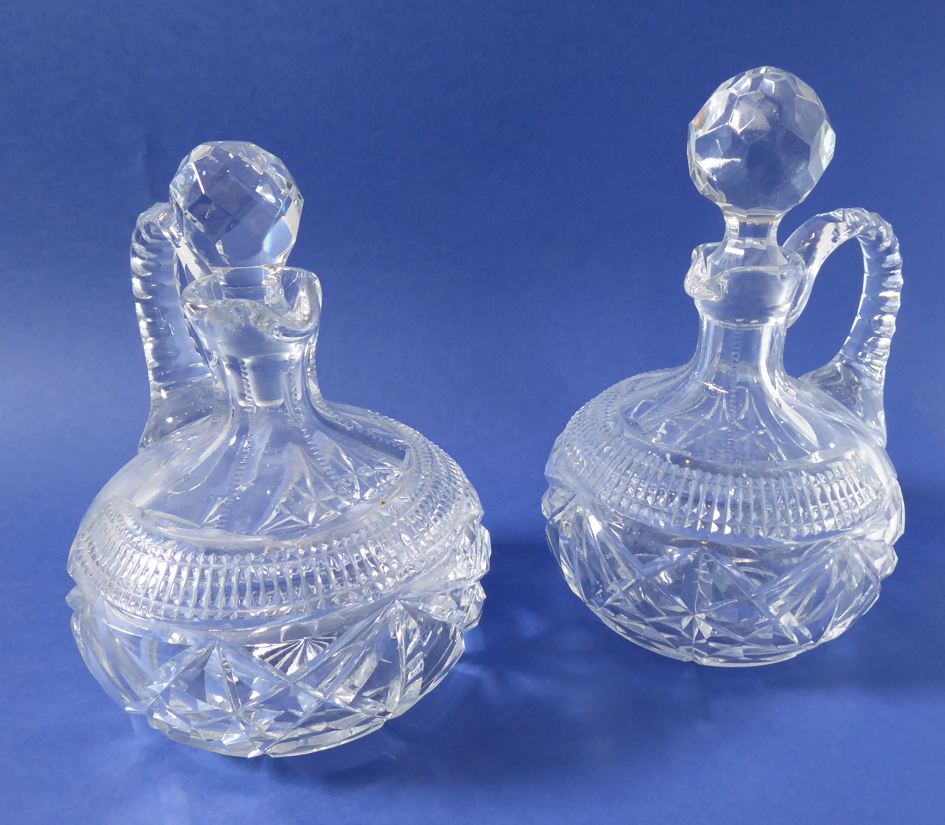 A pair of 19th century cut-glass flasks with arched faceted handles (one stopper replaced)