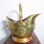 A late 19th century brass coal scuttle; helmet-shaped, hand-beaten and decorated in repoussé style