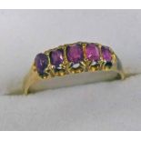 5 STONE RUBY SET RING IN AN UNMARKED YELLOW METAL SCROLL MOUNT