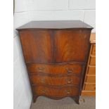MAHOGANY CABINET WITH SHAPED FRONT AND 2 PANEL DOORS OVER 3 DRAWERS ON BRACKET SUPPORTS.