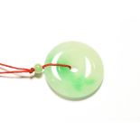 A circular jade pendant, on a red cord necklace, pendant measures 3.7cm diameter . Gross weight 16.7
