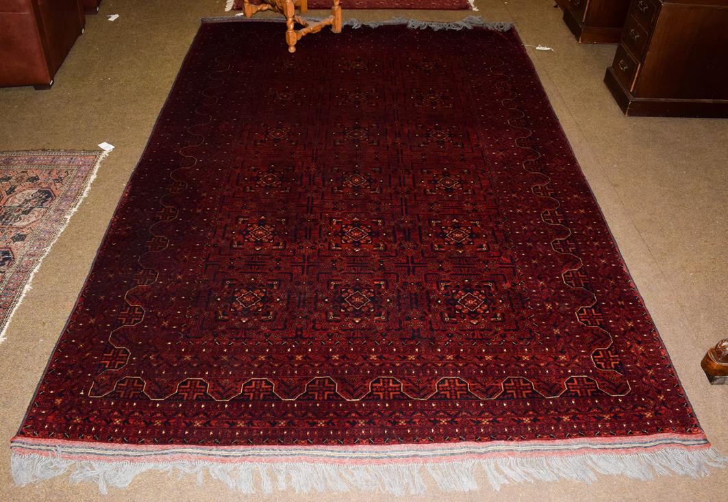 An Afghan Bashir carpet, the deep brick red compartmentalised field enclosed by multiple