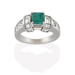 An Emerald and Diamond Ring, the emerald-cut emerald in a white four claw setting, flanked by a trio