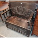 An early 20th century carved oak monks' bench, the pivoting back support above a hinged seat with