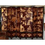 An imposing Chinese eight fold partition screen, decorated in relief with gilt figures and buildings