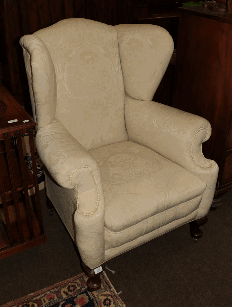 A Georgian style upholstered wingback armchair with scrolling arms and raised on cabriole feet