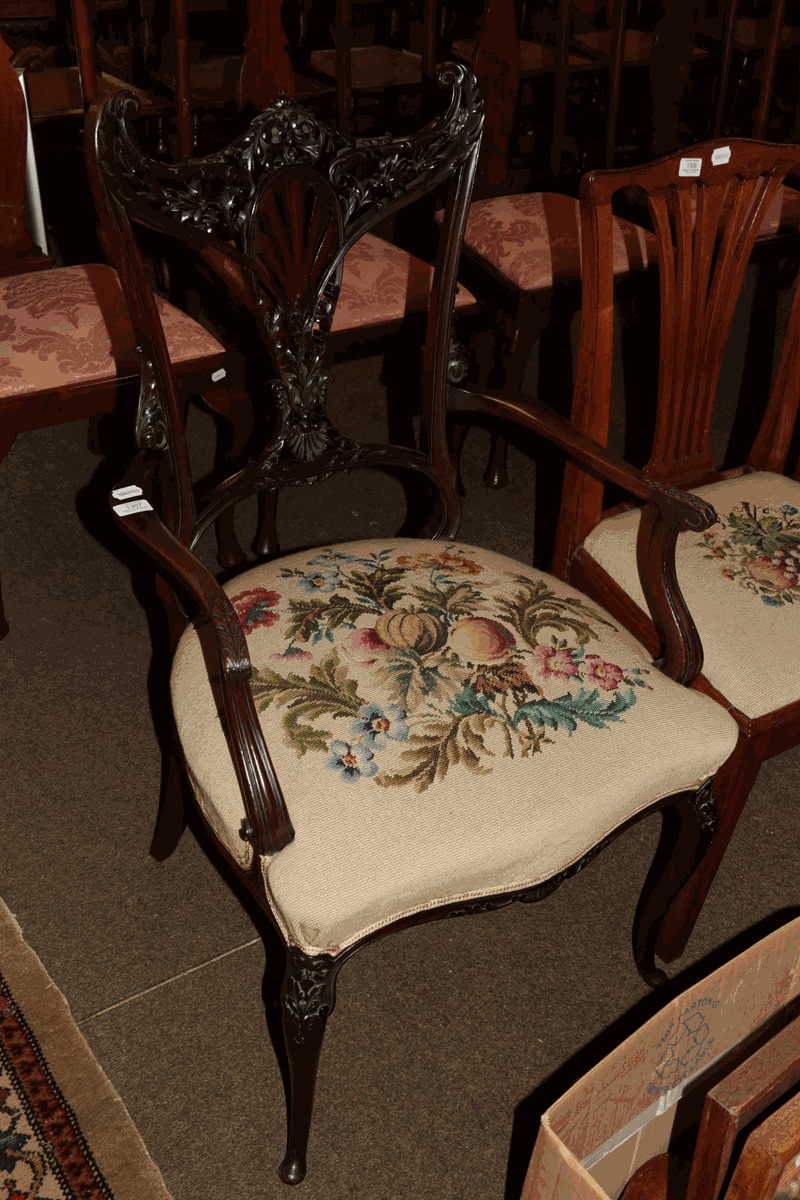 An extensively carved Edwardian mahogany open armchair with needle point seat
