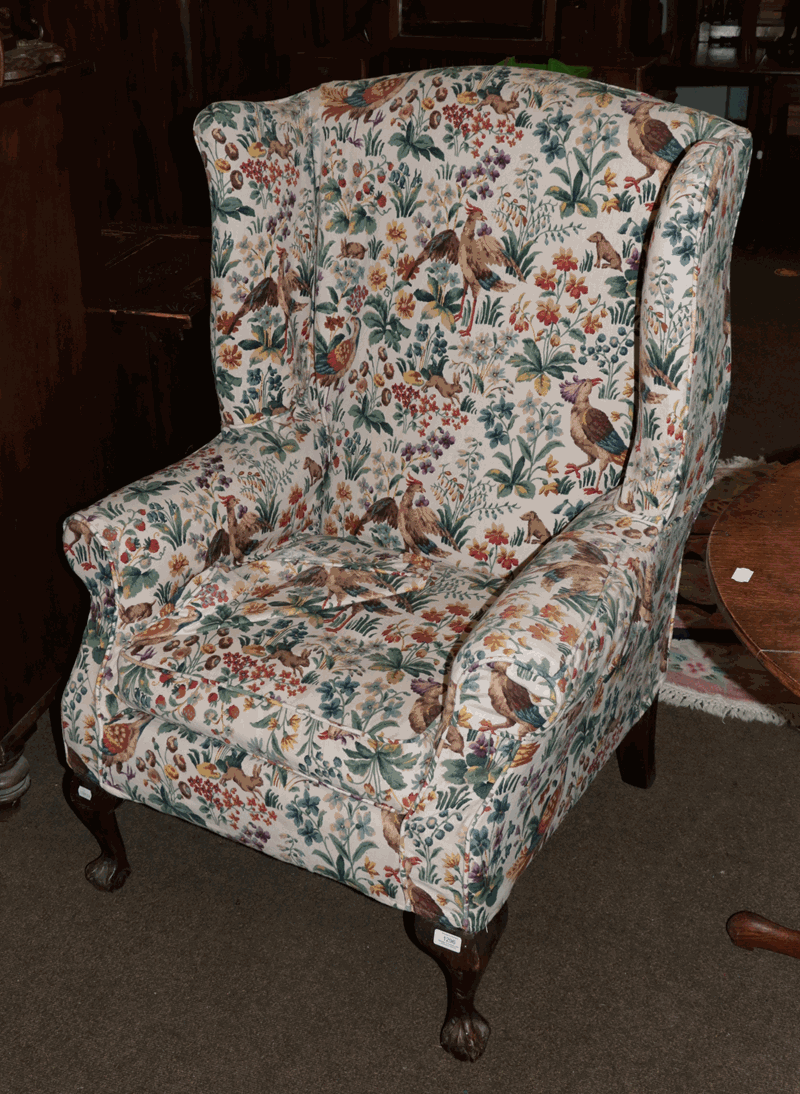 A Georgian style upholstered wing back armchair on ball and claw supports