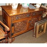 An oak side cabinet with armorial carved panels on bulbous supports with cross stretcher (en suite